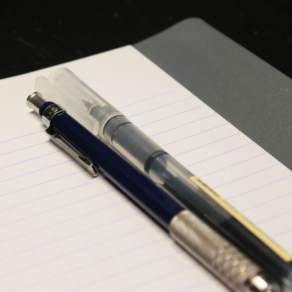 A pencil and pen sitting on notebook paper.